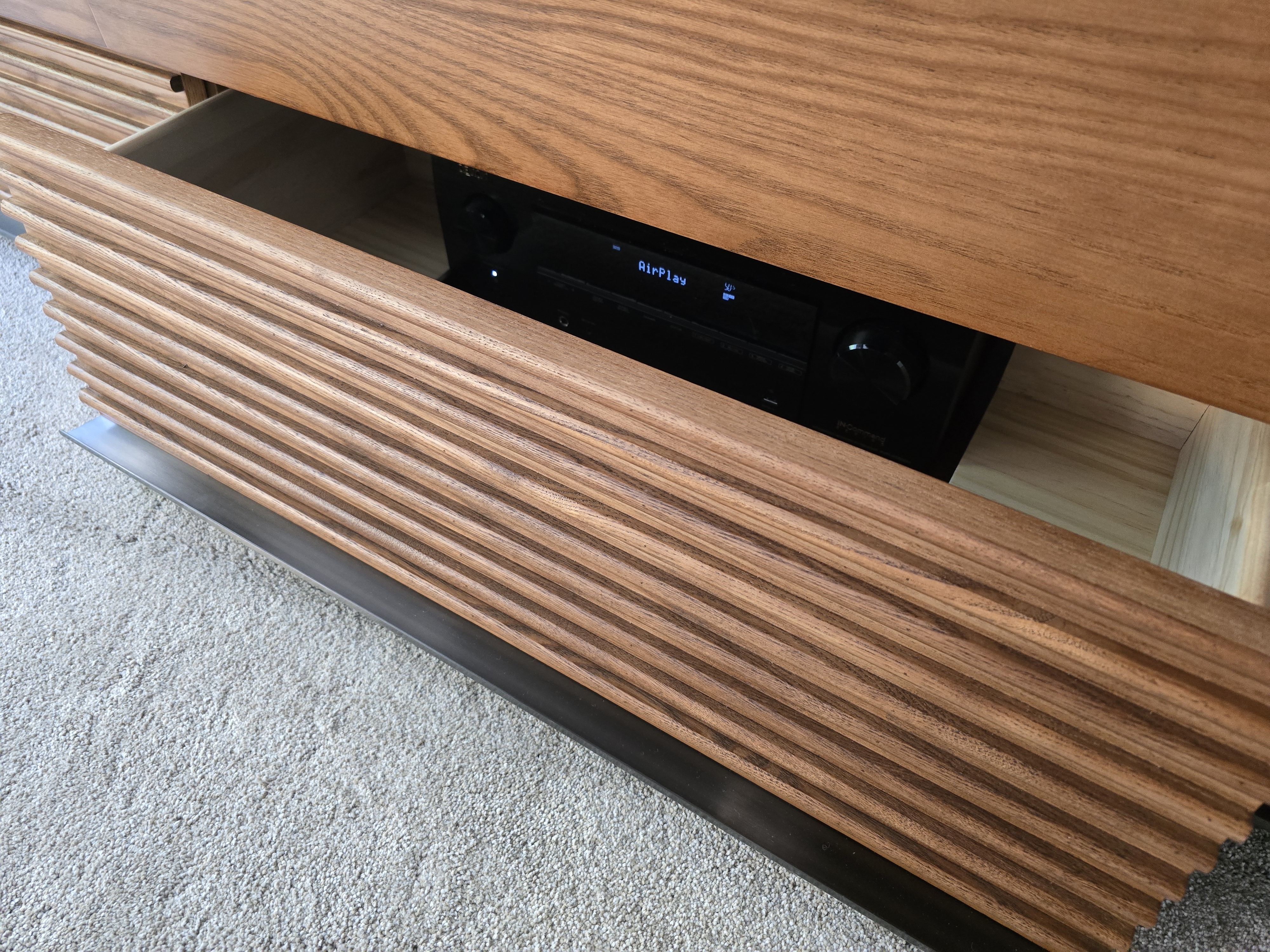 Close-up of the slat-front credenza panels — AV receiver LCD visible through the slats