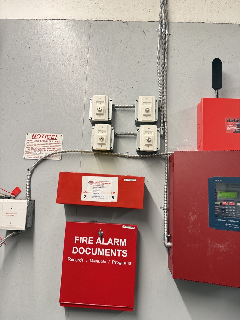 NAPCO/FireLine addressable fire alarm panel installed in a commercial mechanical room with cellular communicator, signage, and document box